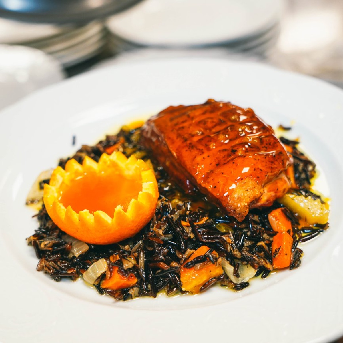A glazed entrée on wild rice with roasted vegetables and a carved orange half