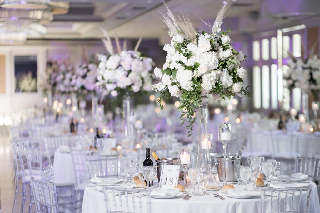 A table in the Encore Ballroom set with tall white flowers, candles and wine