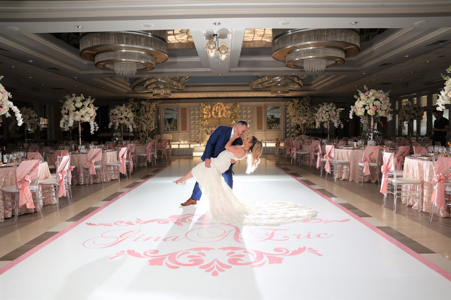 A groom dips his bride on the Encore Ballroom dance floor, pink-draped tables around
