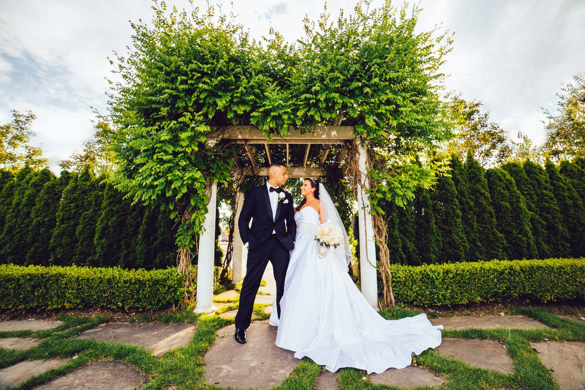 A couple under a vine-covered wooden arbor in Russo’s Garden