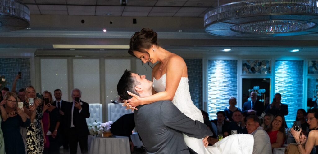 A groom lifts his bride during their first dance over low fog as guests watch