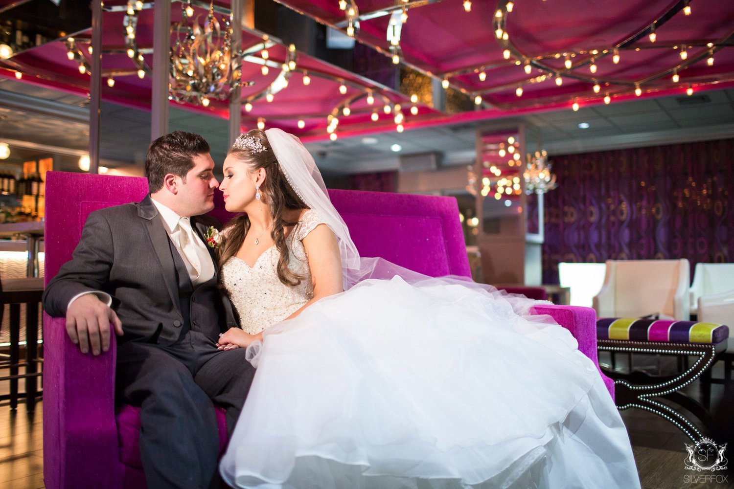 A bride and groom on a magenta sofa in the Rose Lounge