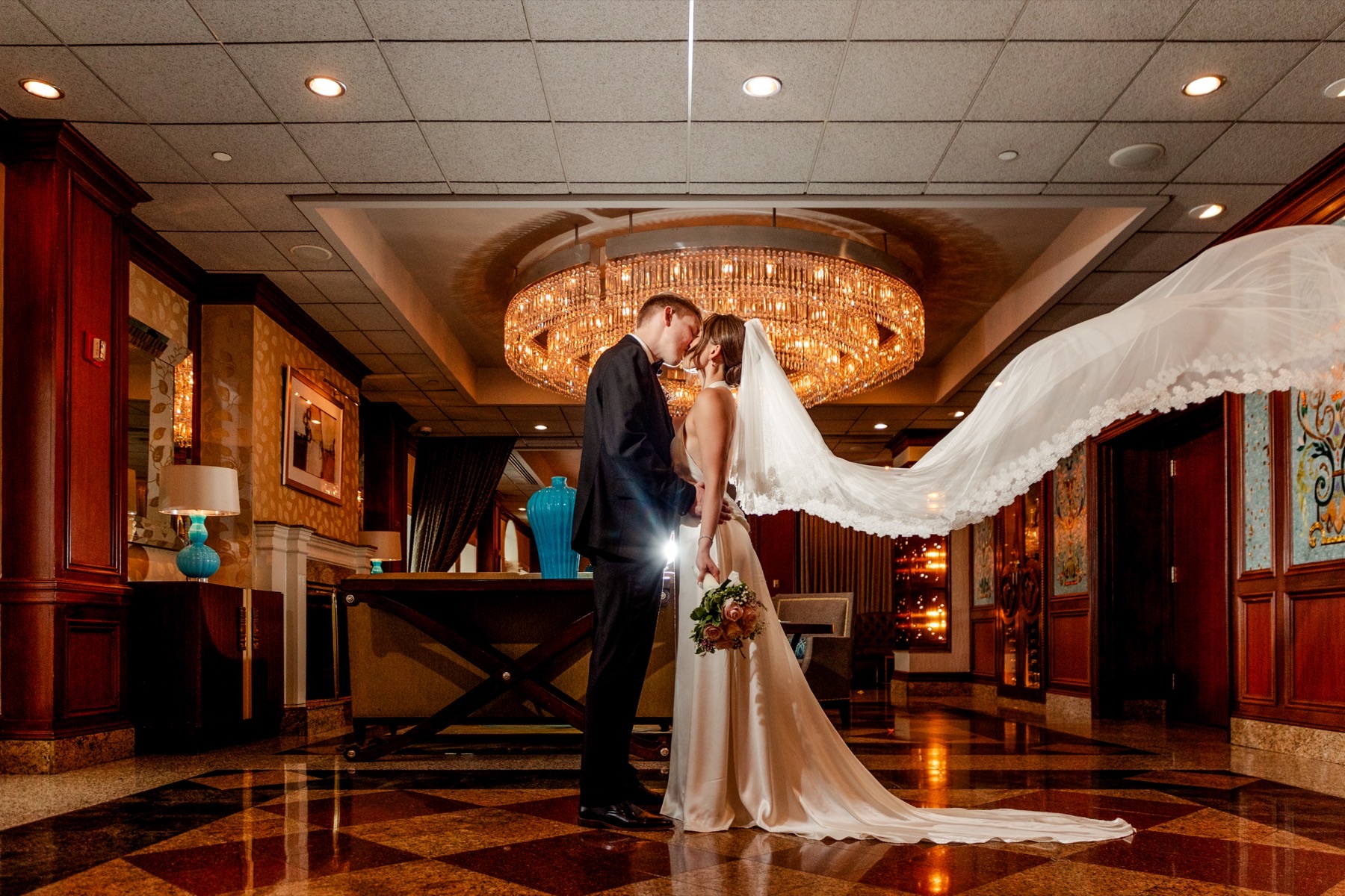 A bride and groom in a wood-paneled foyer, her veil lifting behind her