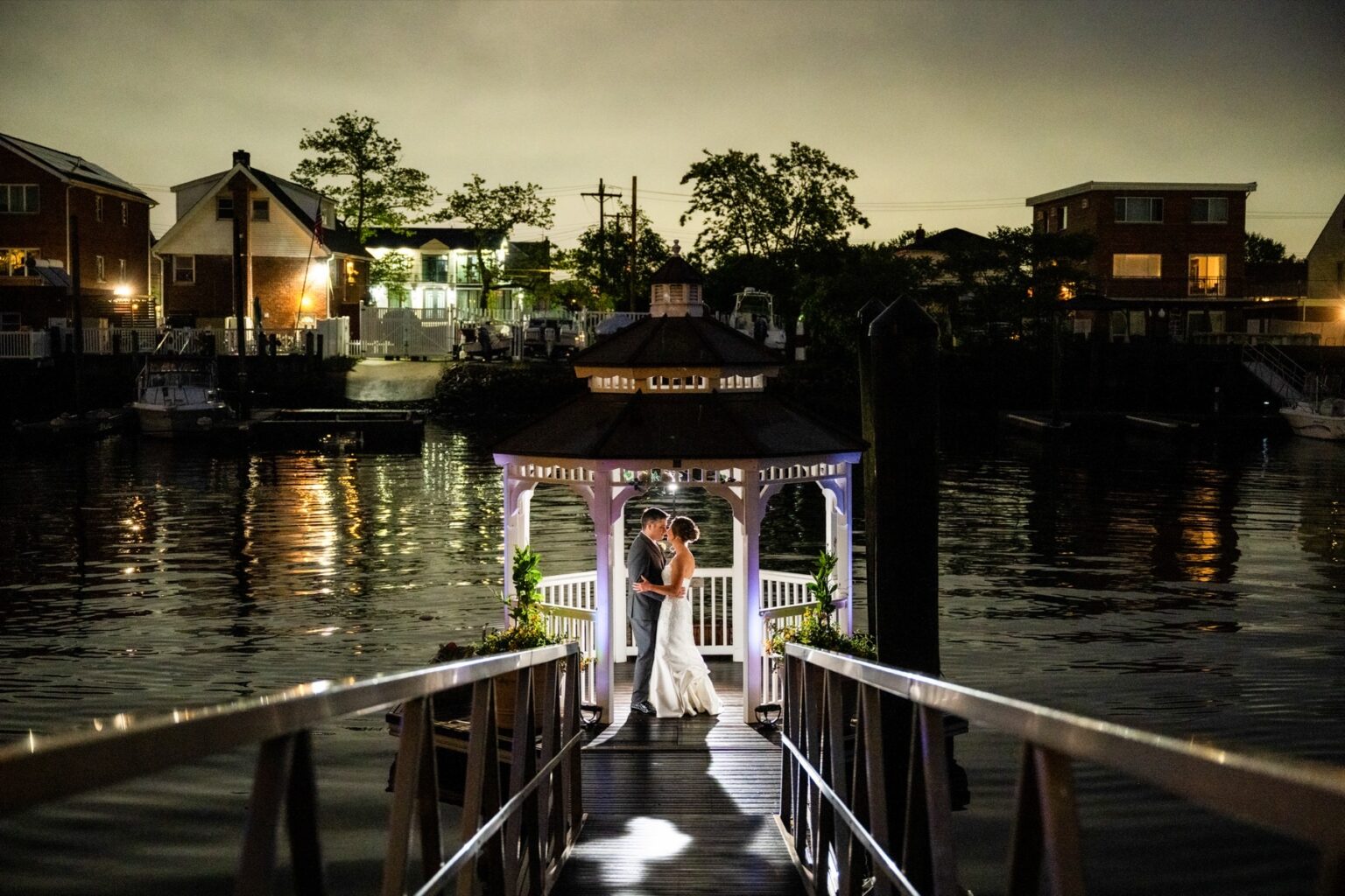 A couple in the lit gazebo over the water at night