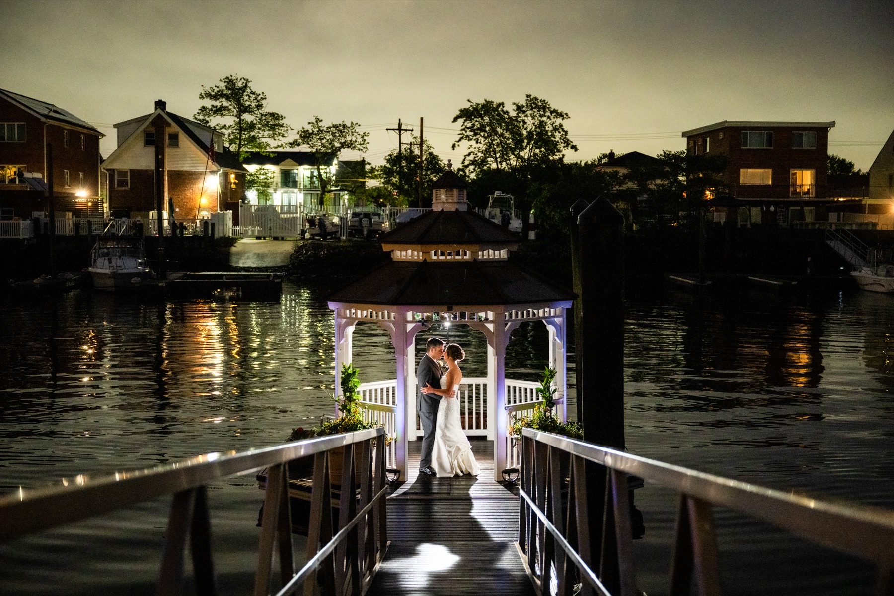 A couple in the lit gazebo over the water at night