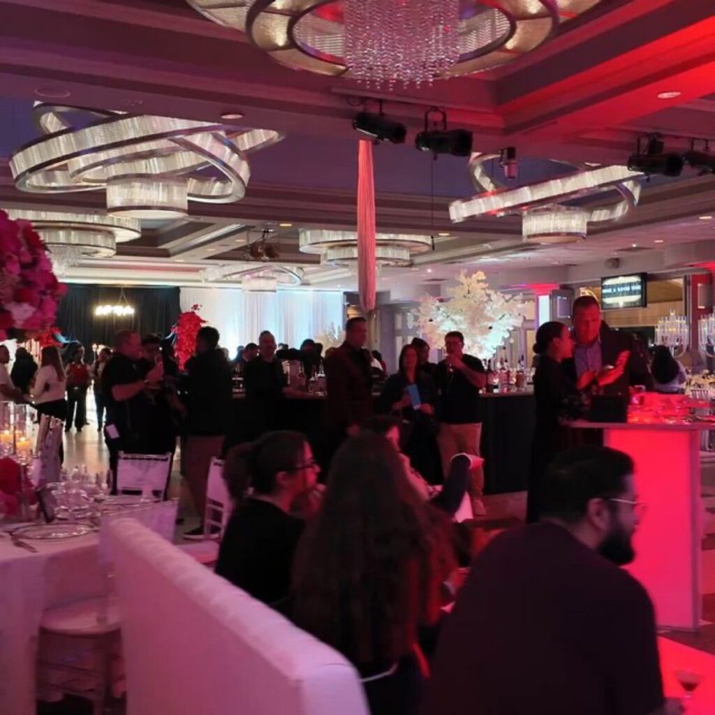Guests gathered in a ballroom under red and pink light and ring chandeliers